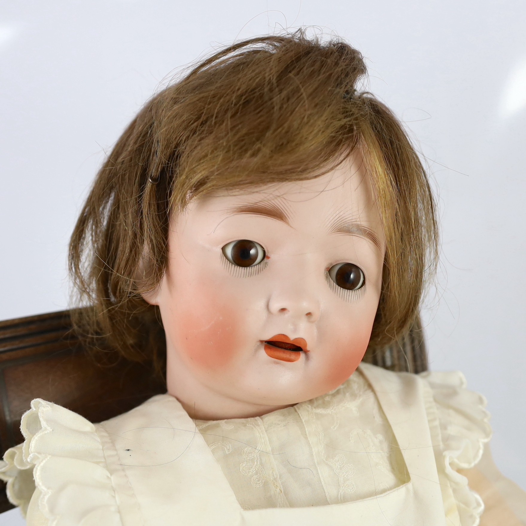 A Kohl and Wengenroth bisque character doll, German, circa 1910, 21in. Please note the chair is for display purposes only.